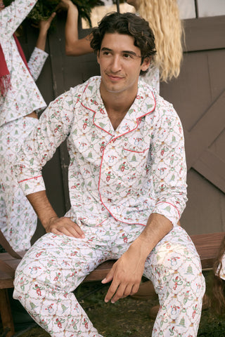 A woman wears a SERFLEX Deck The Halls Bailey Pajamas set featuring a short-sleeved top and shorts with a white background and a repeating Christmas-themed pattern of elves, snowmen, and evergreen trees.