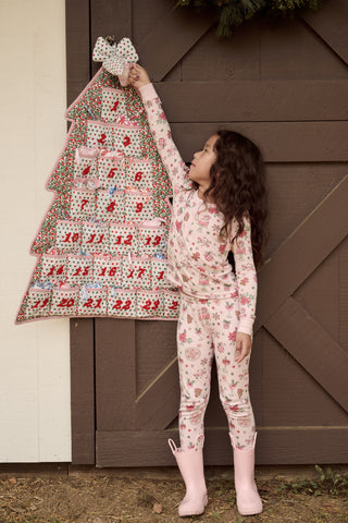 A child in a patterned Kids Seasons Soiree Juniper Pajamas two-piece set and rubber boots sits on a wooden sled and looks through binoculars.