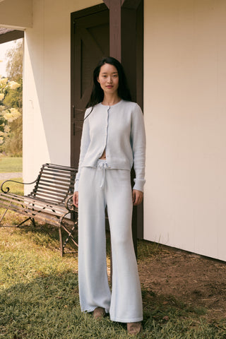 A woman poses with her arms crossed, wearing an icy blue AFFINA Moxie Cardigan with pearl-like buttons and matching drawstring pants.
