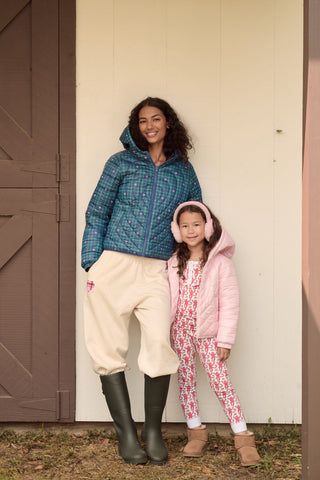 A person wearing a light pink SOPHISTICA Kids Lovely Monkey/Hearts Reversible Puffer Jacket made of durable nylon with repeating heart-shaped quilting and a hood.