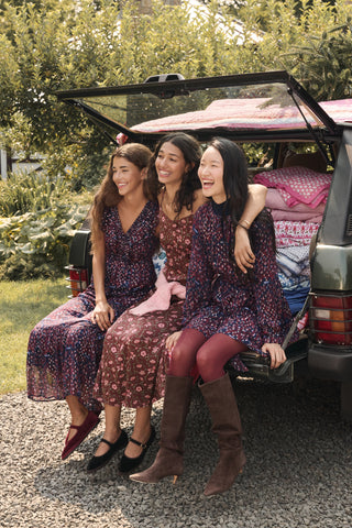 Two girls in matching SOPHISTICA Kids Rhone Ciera dresses stand in front of a dark green SUV with a Christmas tree strapped to the roof.