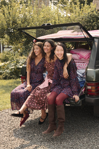 A woman wears a brown silk satin Greta Floral Ditsy Alice Dress with a sweetheart neckline, pink floral ditsy print, and thin straps, paired with brown ankle boots.