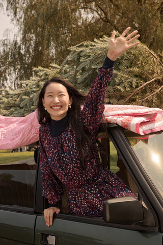 Two girls in matching SOPHISTICA Kids Rhone Ciera dresses stand in front of a dark green SUV with a Christmas tree strapped to the roof.