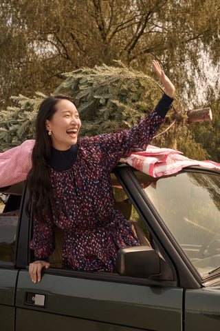 Two girls in matching SOPHISTICA Kids Rhone Ciera dresses stand in front of a dark green SUV with a Christmas tree strapped to the roof.