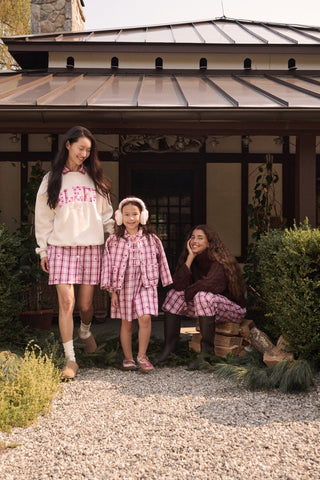 A young girl wearing a pink and white plaid hearts Kids Plaid Hearts Finn Jacket and a matching skirt.