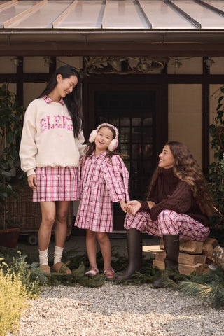 A girl wears a pink and white plaid hearts SAPPHIRE Kids Plaid Hearts Isabelle Dress with long sleeves and light-colored ballet flats.
