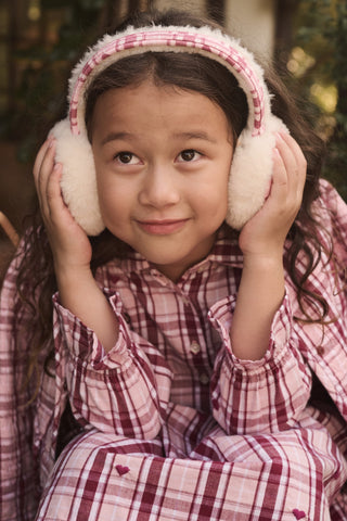 A person wearing LUHE Plaid Hearts Earmuffs in a cozy pink and white plaid pattern with heart details.