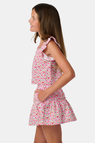 Three young girls sit close together outdoors, each wearing the Roller Rabbit Kids Garden Gate Floral Emmett Top—an ideal choice for girls' summer clothing. They are smiling and appear to be engaged in conversation, with greenery and stone walls in the background.
