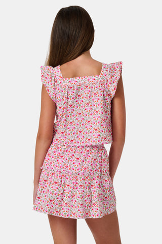 Three young girls sit close together outdoors, each wearing the Roller Rabbit Kids Garden Gate Floral Emmett Top—an ideal choice for girls' summer clothing. They are smiling and appear to be engaged in conversation, with greenery and stone walls in the background.