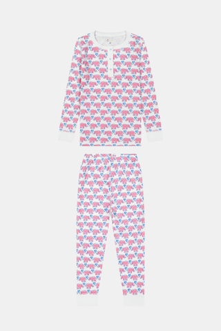 A young girl stands barefoot, smiling with hands on hips, wearing Kids Hathi Hearts Pajamas by Roller Rabbit—soft Pima Cotton pajamas featuring pink and blue elephant patterns on a white background.