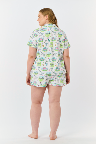 The Roller Rabbit Game, Set, Monkey Polo Pajamas is a two-piece set featuring a short-sleeve button-up shirt and matching shorts. Crafted from soft Pima Cotton, the white fabric is adorned with a playful cartoon animal and house print in green, blue, and yellow tones.