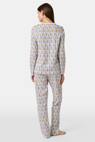 A person stands barefoot wearing the SERFLEX Vanderbilt Lovely Monkey Pajamas, a matching long-sleeve set featuring an allover cartoon animal print. The background is plain and light gray.