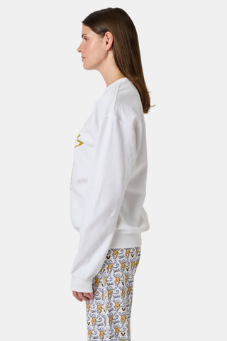 A woman wearing a white FANFAB Vanderbilt Lovely Monkey Crewneck cotton fleece sweatshirt featuring a large V and Go Dores text, paired with white patterned pajama pants, stands against a plain background.