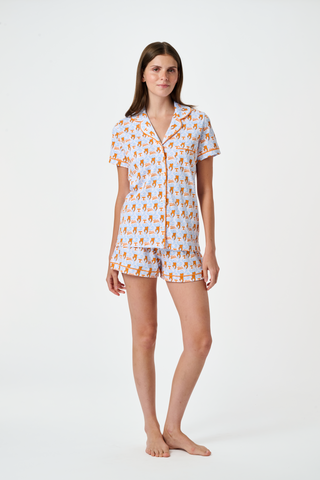 A woman stands barefoot against a plain white background wearing SERFLEX’s Tennessee Lovely Monkey Pajamas: a matching white women’s set with an all-over orange and brown monkey print, featuring long sleeves and full-length pants.