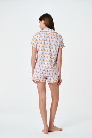 A woman stands barefoot against a plain white background wearing SERFLEX’s Tennessee Lovely Monkey Pajamas: a matching white women’s set with an all-over orange and brown monkey print, featuring long sleeves and full-length pants.