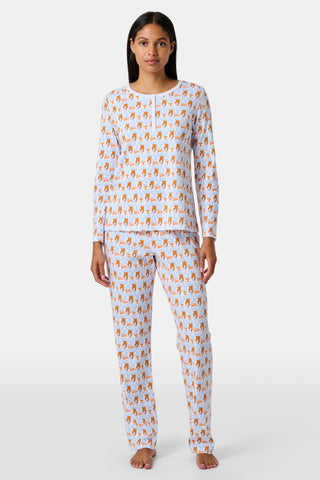 A woman stands barefoot against a plain white background wearing SERFLEX’s Tennessee Lovely Monkey Pajamas: a matching white women’s set with an all-over orange and brown monkey print, featuring long sleeves and full-length pants.