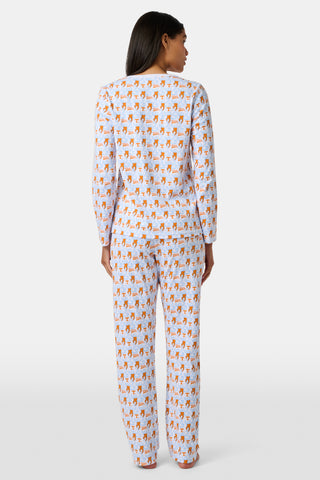 A woman stands barefoot against a plain white background wearing SERFLEX’s Tennessee Lovely Monkey Pajamas: a matching white women’s set with an all-over orange and brown monkey print, featuring long sleeves and full-length pants.