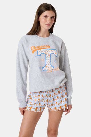 A woman stands facing forward with a neutral expression, wearing the FANFAB Tennessee Crewneck in gray and white shorts featuring an orange and blue pattern, her hand casually tucked into her shorts pocket as she shows off her school pride.