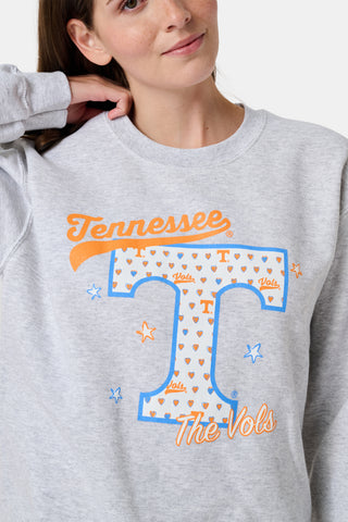 A woman stands facing forward with a neutral expression, wearing the FANFAB Tennessee Crewneck in gray and white shorts featuring an orange and blue pattern, her hand casually tucked into her shorts pocket as she shows off her school pride.