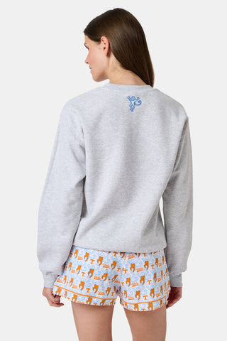 A woman stands facing forward with a neutral expression, wearing the FANFAB Tennessee Crewneck in gray and white shorts featuring an orange and blue pattern, her hand casually tucked into her shorts pocket as she shows off her school pride.