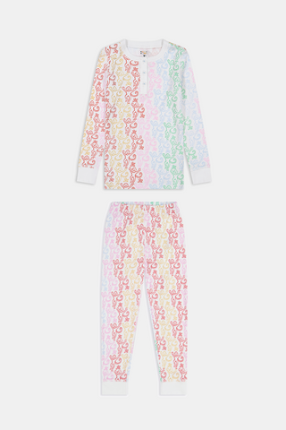 A girl with long brown hair stands barefoot, smiling and facing forward in Roller Rabbit Kids Monkey Juniper Pajamas—a matching set with a playful monkey print—against a plain white background.