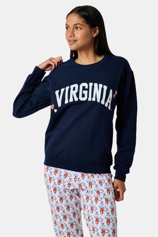 A woman stands to the side with one hand in her hair, wearing the FANFAB UVA Crewneck in navy blue paired with white pajama pants featuring an orange and blue pattern.