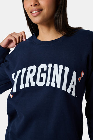 A woman stands to the side with one hand in her hair, wearing the FANFAB UVA Crewneck in navy blue paired with white pajama pants featuring an orange and blue pattern.