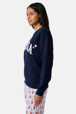 A woman stands to the side with one hand in her hair, wearing the FANFAB UVA Crewneck in navy blue paired with white pajama pants featuring an orange and blue pattern.