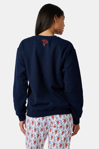 A woman stands to the side with one hand in her hair, wearing the FANFAB UVA Crewneck in navy blue paired with white pajama pants featuring an orange and blue pattern.