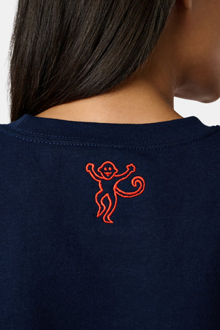 A woman stands to the side with one hand in her hair, wearing the FANFAB UVA Crewneck in navy blue paired with white pajama pants featuring an orange and blue pattern.