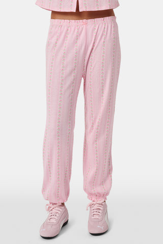 The Kids Daisy Heart Stripe Lucy Pants by Roller Rabbit are crafted from soft Pima cotton genie pant fabric in rose pink, featuring an elastic waistband and cuffs, with a subtle striped pattern and small floral designs throughout—making them a charming addition to girls' fashion.