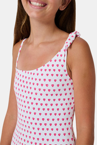 The Roller Rabbit Hearts Kids Jacey One Piece is a swimsuit with an asymmetrical neckline, white fabric dotted with pink hearts, and an adjustable knot-tied shoulder strap.