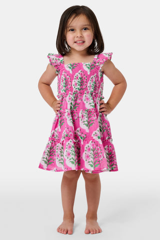 The Kids Ava Floral Ceri Dress by Roller Rabbit is a sleeveless baby dress featuring a smocked bodice and ruffled straps, adorned with green and white leaf patterns on a vibrant pink background, and comes with matching bloomers.