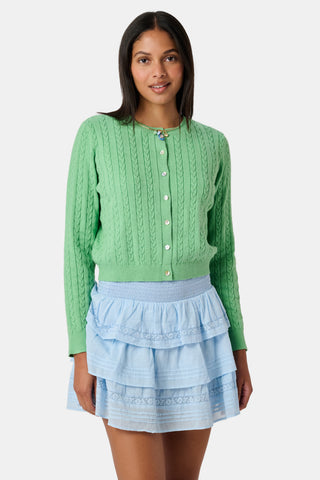 The Roller Rabbit Cable Stripe Moxie Cardigan is a bright forest green, long-sleeve cardigan featuring a cable-knit design. Crafted from soft cotton cashmere, it has a crew neckline and gold buttons down the front, shown against a plain white background.