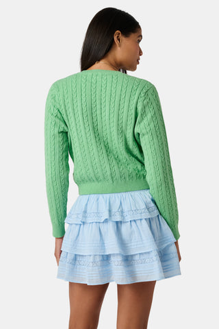 The Roller Rabbit Cable Stripe Moxie Cardigan is a bright forest green, long-sleeve cardigan featuring a cable-knit design. Crafted from soft cotton cashmere, it has a crew neckline and gold buttons down the front, shown against a plain white background.