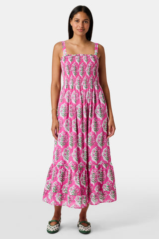 The Kids Ava Floral Ceri Dress by Roller Rabbit is a sleeveless baby dress featuring a smocked bodice and ruffled straps, adorned with green and white leaf patterns on a vibrant pink background, and comes with matching bloomers.
