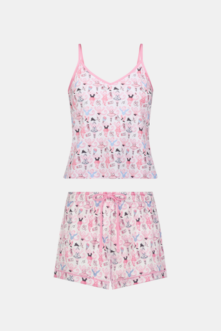 A woman wearing the Roller Rabbit Monkey Pirouette Mischa Set—pink and white cat-print Pima cotton loungewear—and holding a matching bag stands in front of white lockers, smiling slightly at the camera.