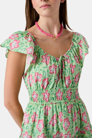 The Kids Verdant Floral Ryan Dress by Roller Rabbit is a green dress for little ones, showcasing pink and white hibiscus flowers in a floral block print. It features ruffled sleeves, a matching diaper cover, and is crafted from soft cotton for comfortable pullover wear.