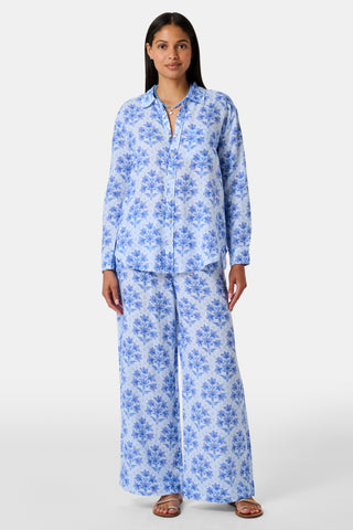 Close-up of the light blue Indigo Garden Paige Pant by Roller Rabbit, featuring a repeating pattern of darker blue floral designs and small star-like shapes. The fabric appears slightly wrinkled.