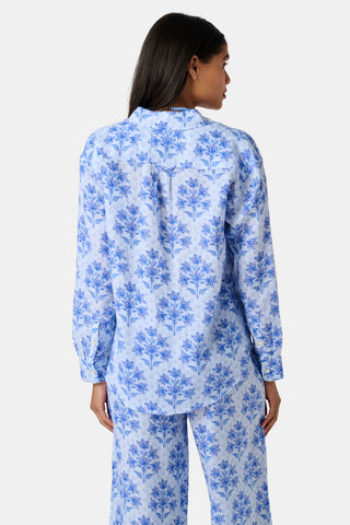 Close-up of the light blue Indigo Garden Paige Pant by Roller Rabbit, featuring a repeating pattern of darker blue floral designs and small star-like shapes. The fabric appears slightly wrinkled.