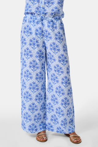 A woman stands against a plain light background wearing the Roller Rabbit Indigo Garden Boyfriend Shirt, a button-up long-sleeve pajama top in a blue floral print paired with matching wide-leg pants.