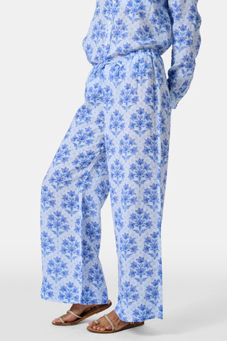A woman stands against a plain light background wearing the Roller Rabbit Indigo Garden Boyfriend Shirt, a button-up long-sleeve pajama top in a blue floral print paired with matching wide-leg pants.
