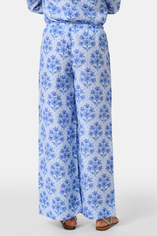 A woman stands against a plain light background wearing the Roller Rabbit Indigo Garden Boyfriend Shirt, a button-up long-sleeve pajama top in a blue floral print paired with matching wide-leg pants.