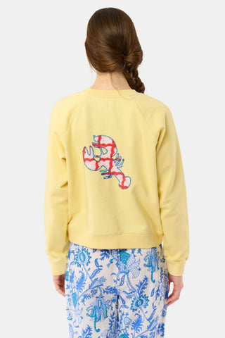 A woman with long brown hair in a braid wears the Roller Rabbit Boston Applique Crewneck and white and blue floral pants, standing against a plain light background.