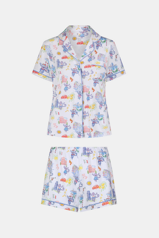 A woman with long dark hair wears Roller Rabbit’s Italy Monkey Polo Pajamas, a playful Pima Cotton set featuring cartoon animals and Italian motifs. The short-sleeved, button-up top pairs perfectly with the matching shorts.