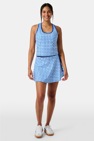 Wearing the Roller Rabbit Gingham Hearts Coco Wrap Skirt, a woman stands next to a net outdoors, surrounded by green grass and trees.