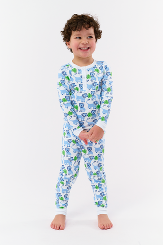 A young child with curly hair smiles barefoot against a plain white background while wearing Kids Leo The Lion Pajamas, crafted from soft Pima cotton.