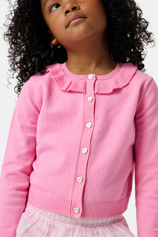 The Kids Ellis Cardigan by Roller Rabbit is a rose pink, long-sleeve cardigan featuring a ruffled collar and pearl-like buttons. Shown flat on a white background, it's made from soft cotton sweater material.