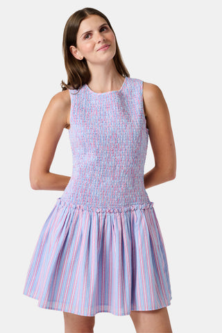 A young girl wearing the Roller Rabbit Kids Sweet Stripe Casey Dress stands in front of lockers, smiling and holding a folder decorated with colorful raindrops.