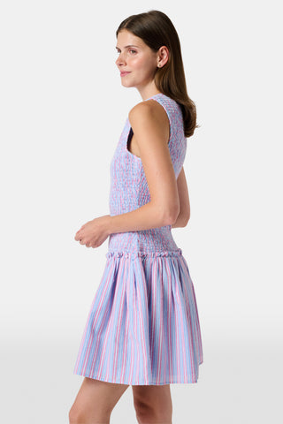 A young girl wearing the Roller Rabbit Kids Sweet Stripe Casey Dress stands in front of lockers, smiling and holding a folder decorated with colorful raindrops.